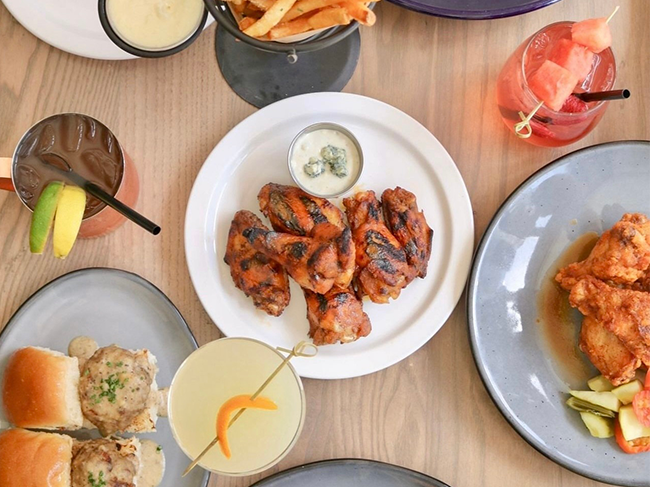 Table full of cocktails and appetizers including wings with ranch